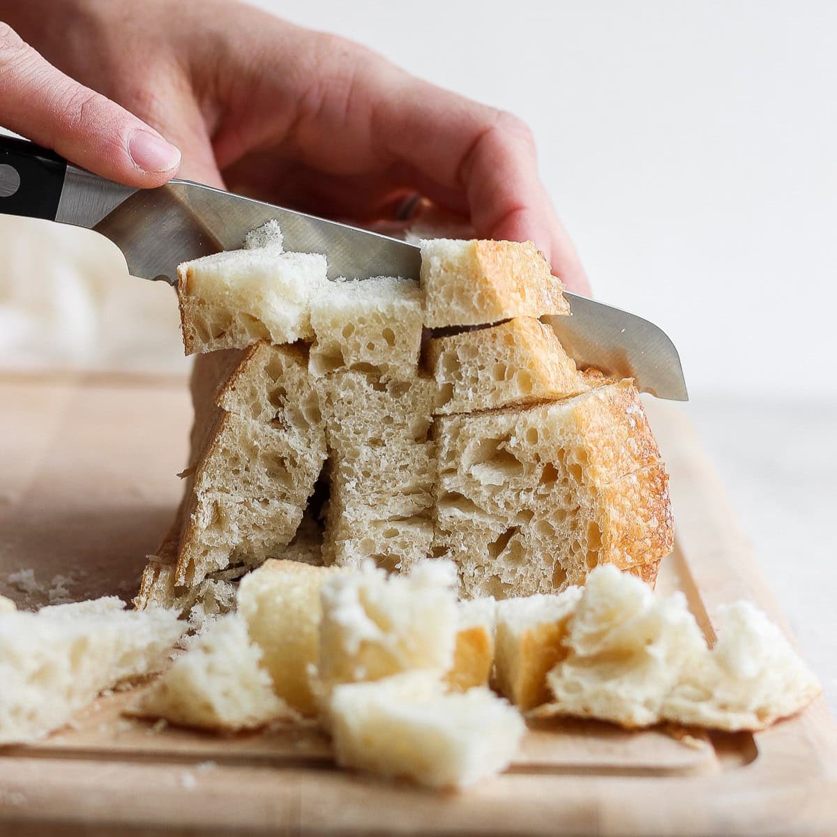 Bread knife cutting bread slices into cubes.