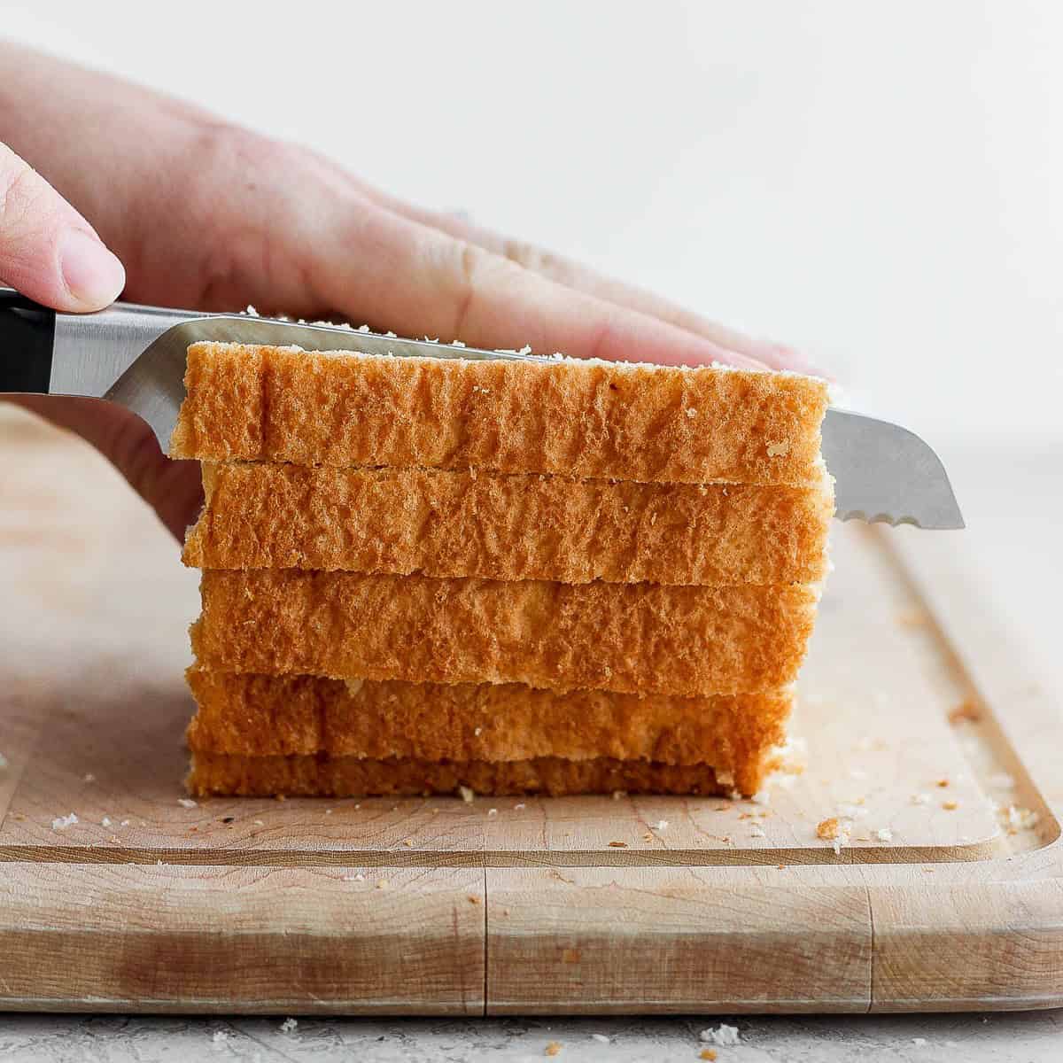 Stack of bread slices on a cutting board being sliced into strips.