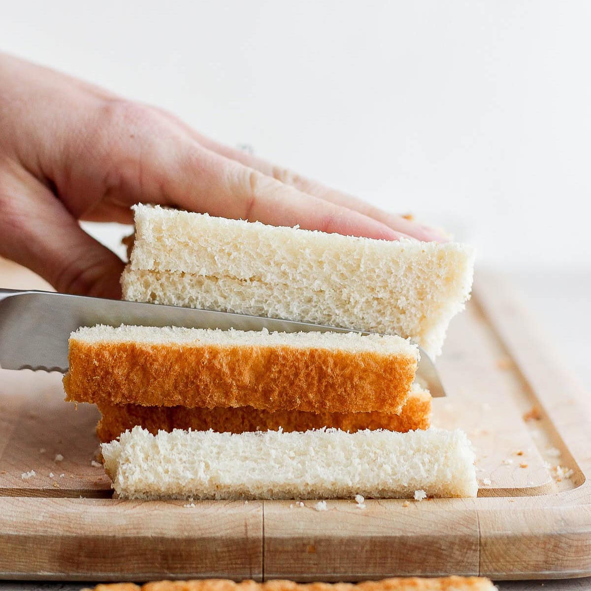 Stack of bread slices on a cutting board being cut in to strips.
