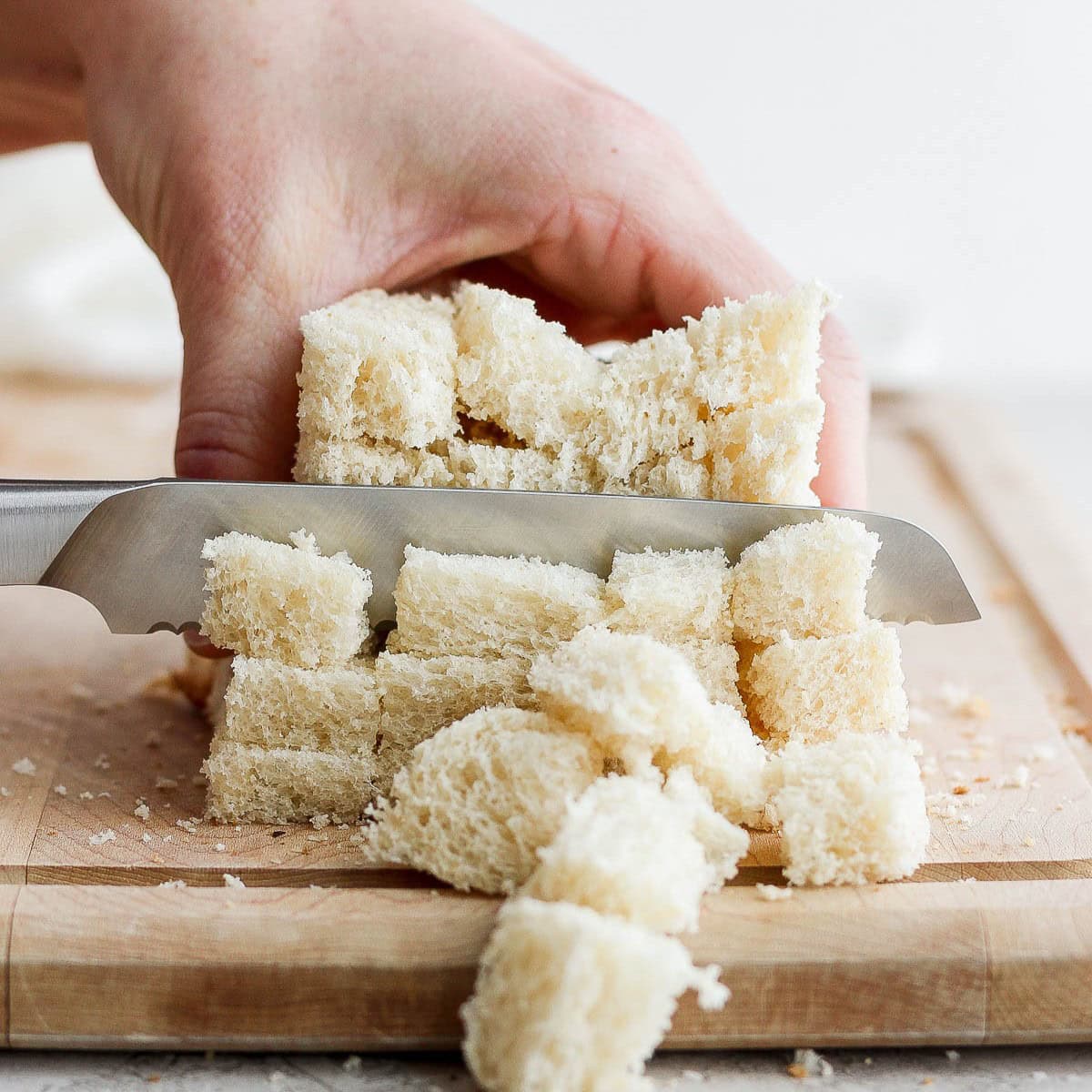 Stack of bread slices on a cutting board being cut into cubes.