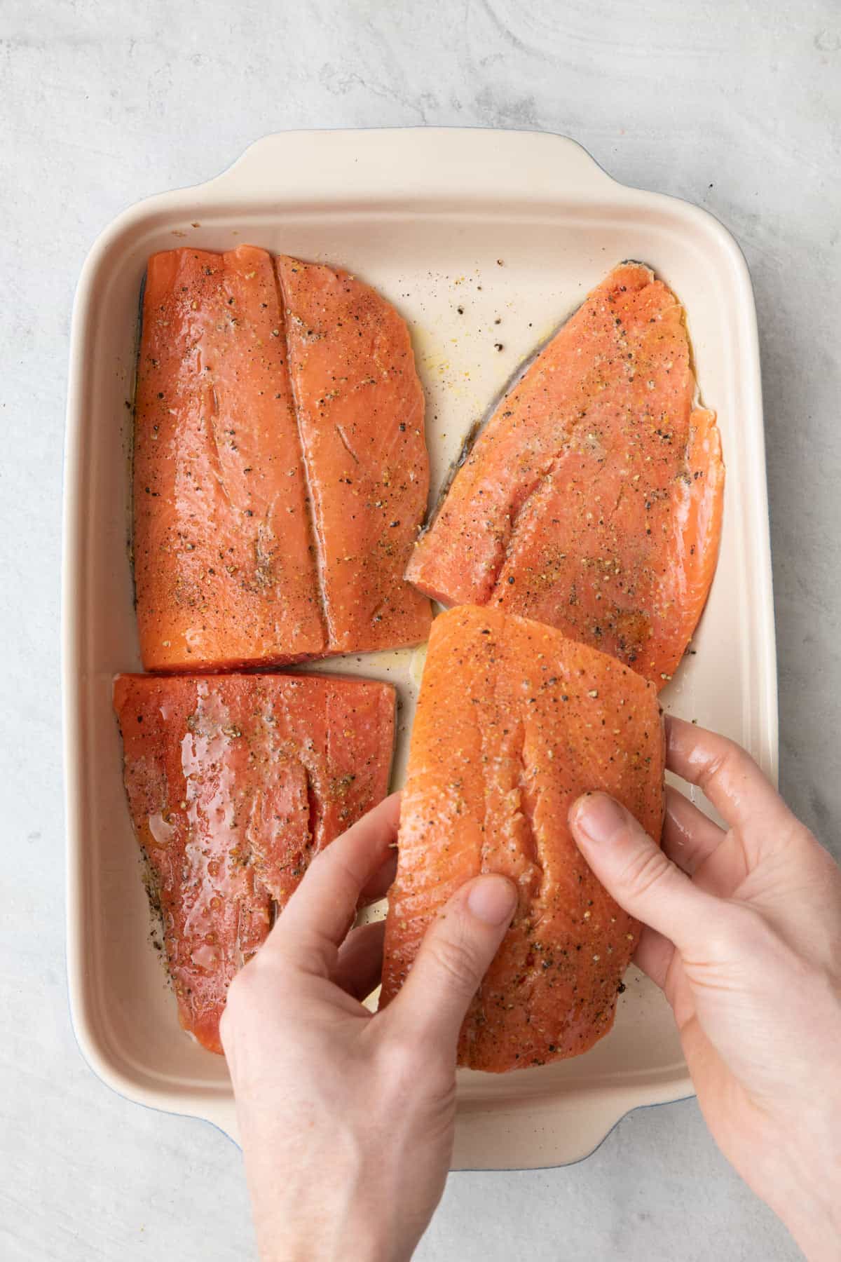Hands coating salmon with oil mixture.