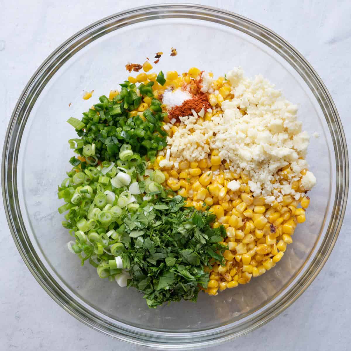 Corn, oil, spices, garlic, cojita cheese, and chopped cilantro, jalapeno, and green onion added to bowl before mixing.