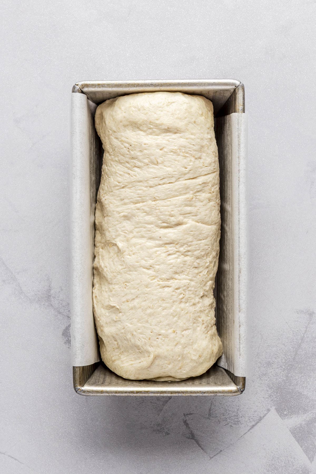 Dough log placed seam side down in parchment lined loaf pan before rising.