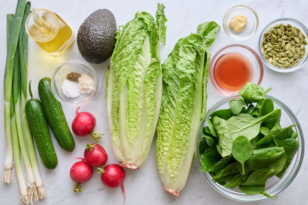 Ingredients: green onions, Persian cucumbers, oil, avocado, seasonings, radishes, romaine, red wine vinegar, Dijon mustard, pumpkin seeds, and spinach.
