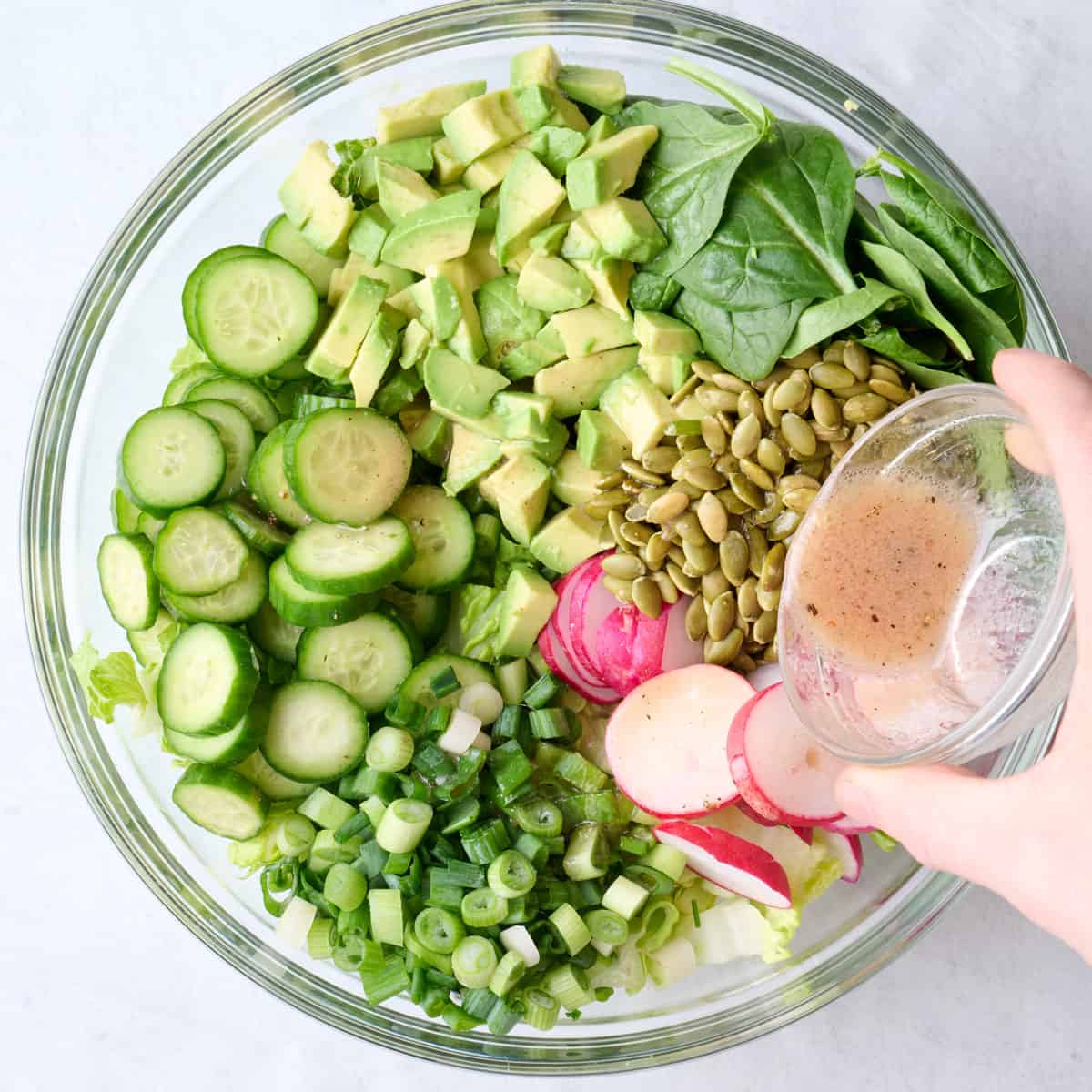 Salad ingredients in a large bowl with salad dressing being poured on top.