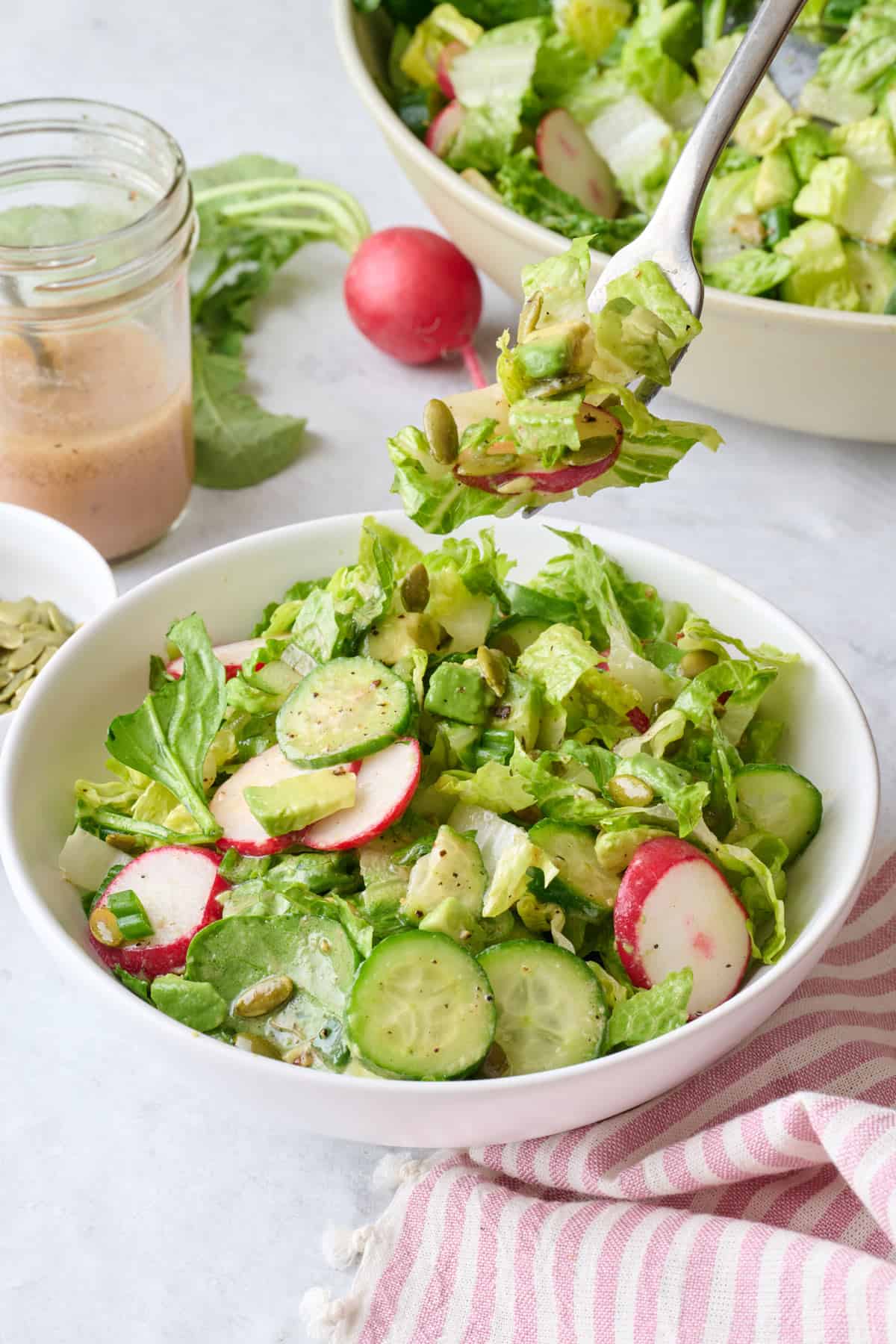 Fork lifting up a bite of a simple green salad from a salad bowl.