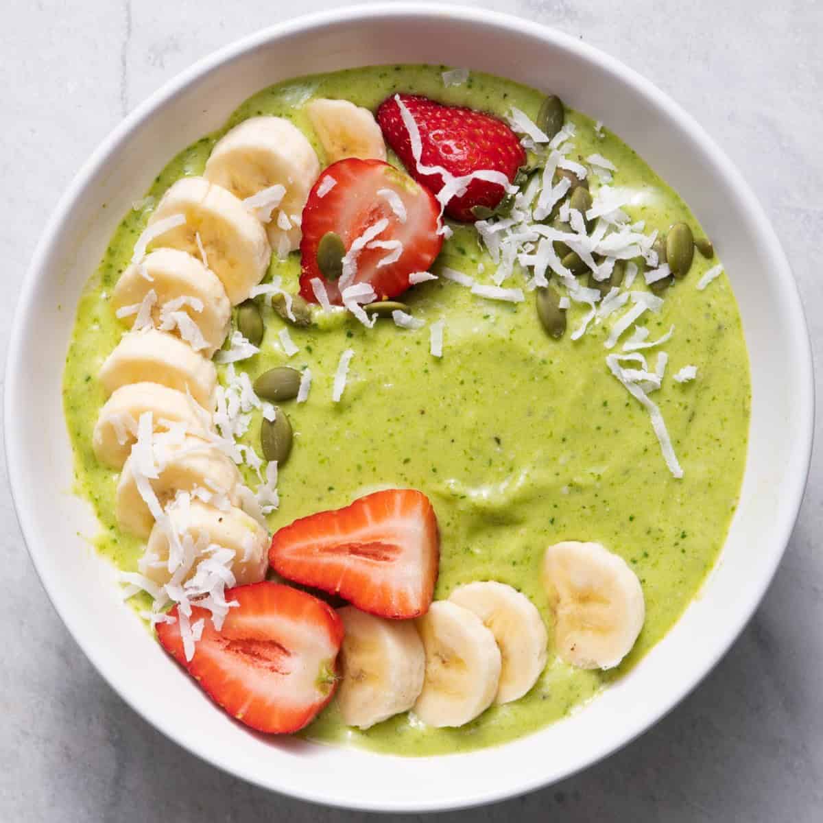 Sweet green smoothie bowl topped with fresh fruit and shredded coconut.