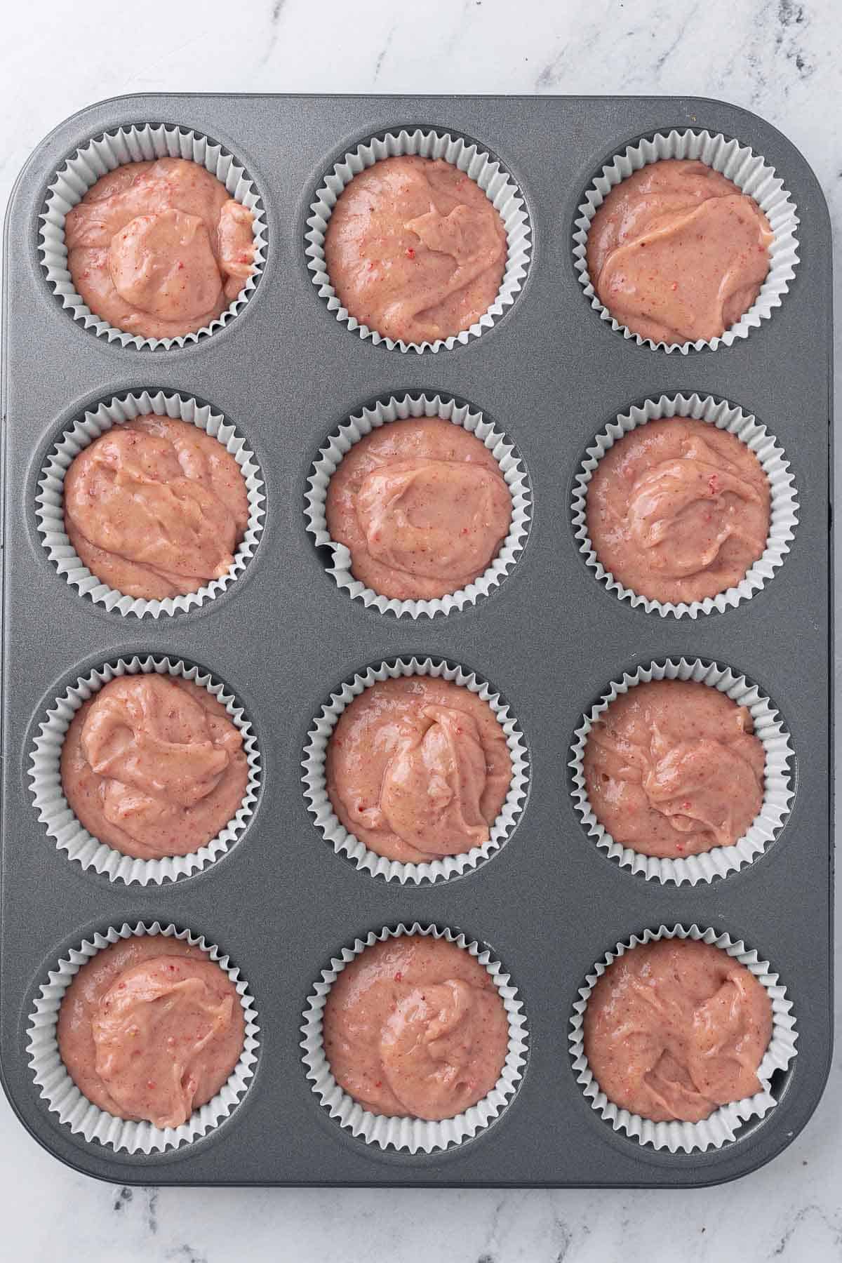 Recipe batter divided into a 12 cup muffin pan with cupcake liners.