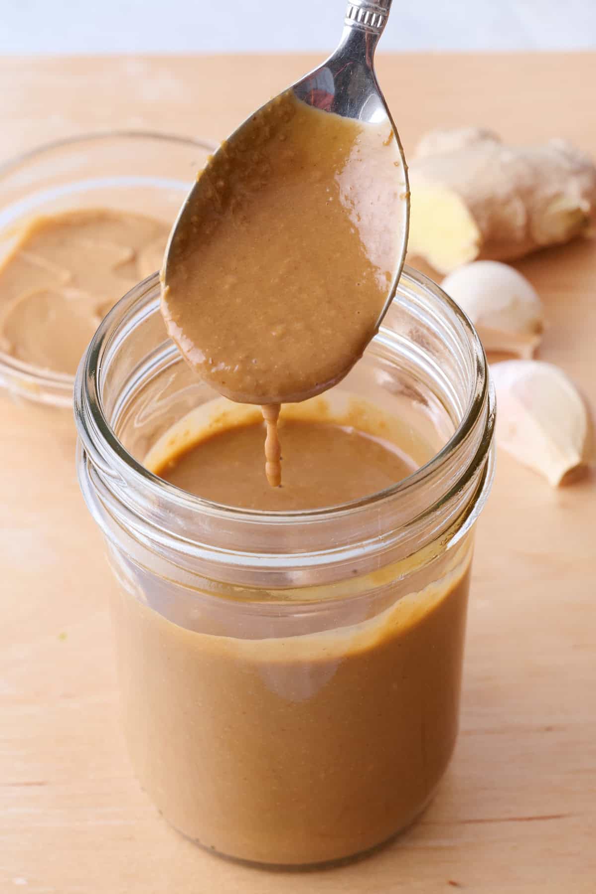 Creamy Thai Peanut Dressing in a jar with a spoon drizzling some over.