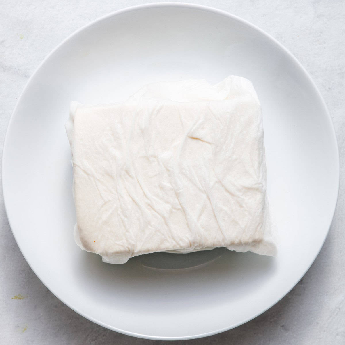 Tofu wrapped in paper towel placed on a plate.