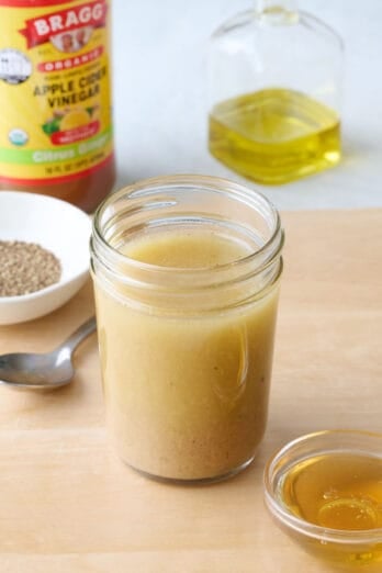 Easy apple cider vinaigrette in a small jar with extra ingredients around.