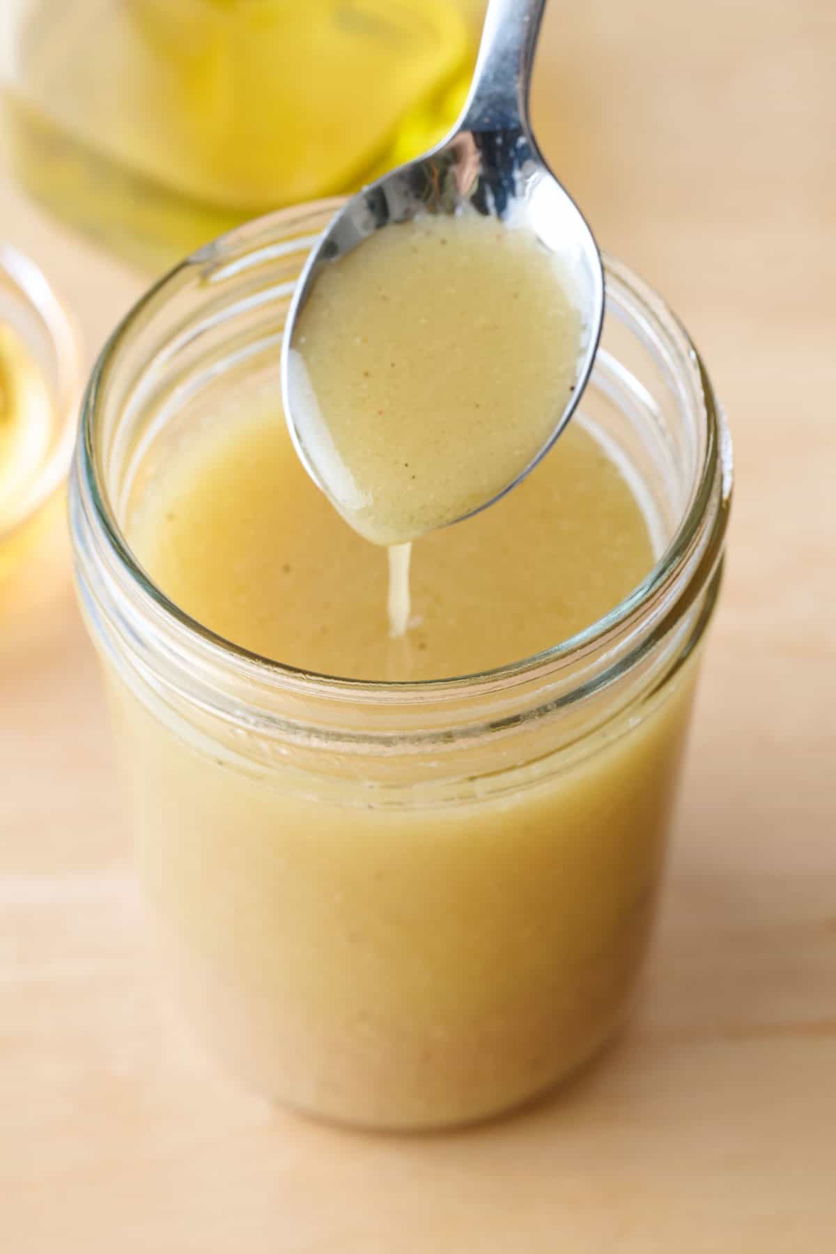 Spoon drizzling apple cider vinaigrette into jar of dressing.