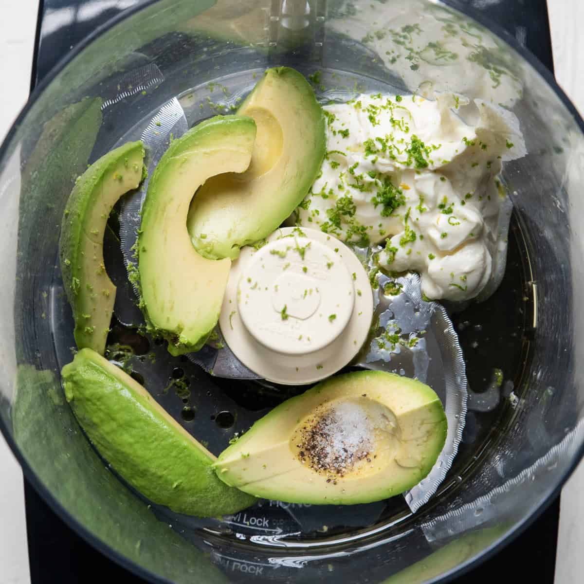 Avocado crema ingredients in the bowl of a food processor before processing.