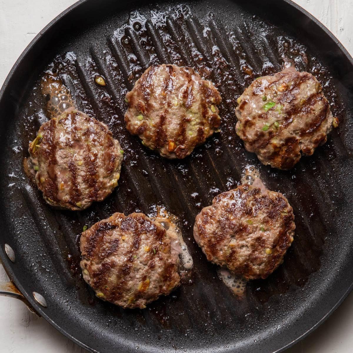 Pan grilled beef burger patties with avocado on a grill pan after cooking.