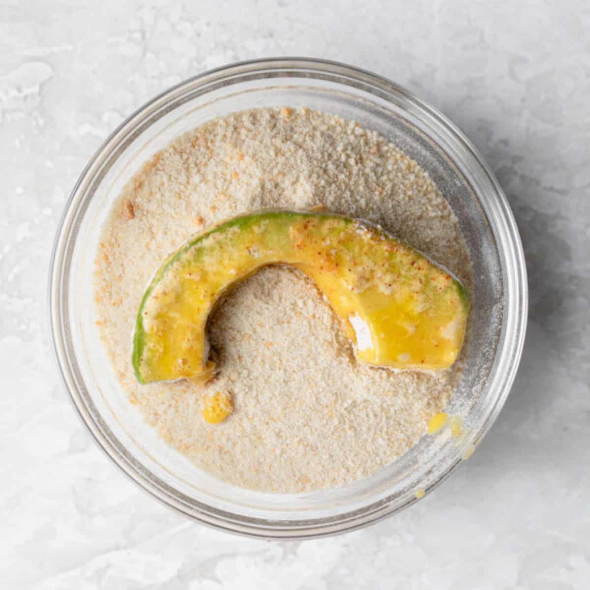 Egg wash coated avocado on top of breadcrumbs.