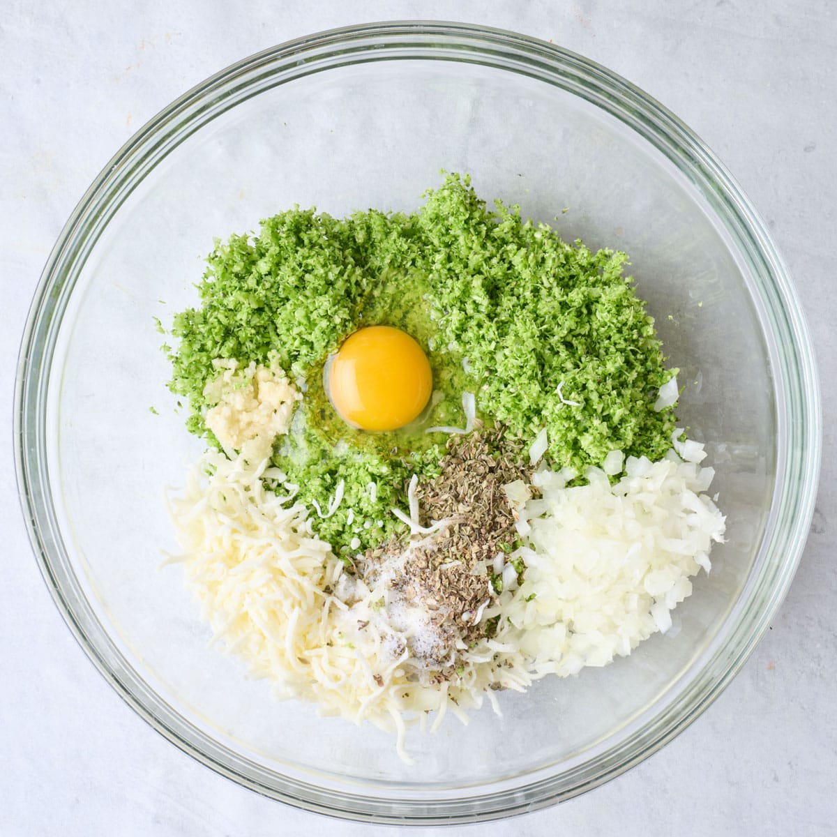 Grated broccoli, egg, onions, garlic, cheese and seasoning in a large bowl.