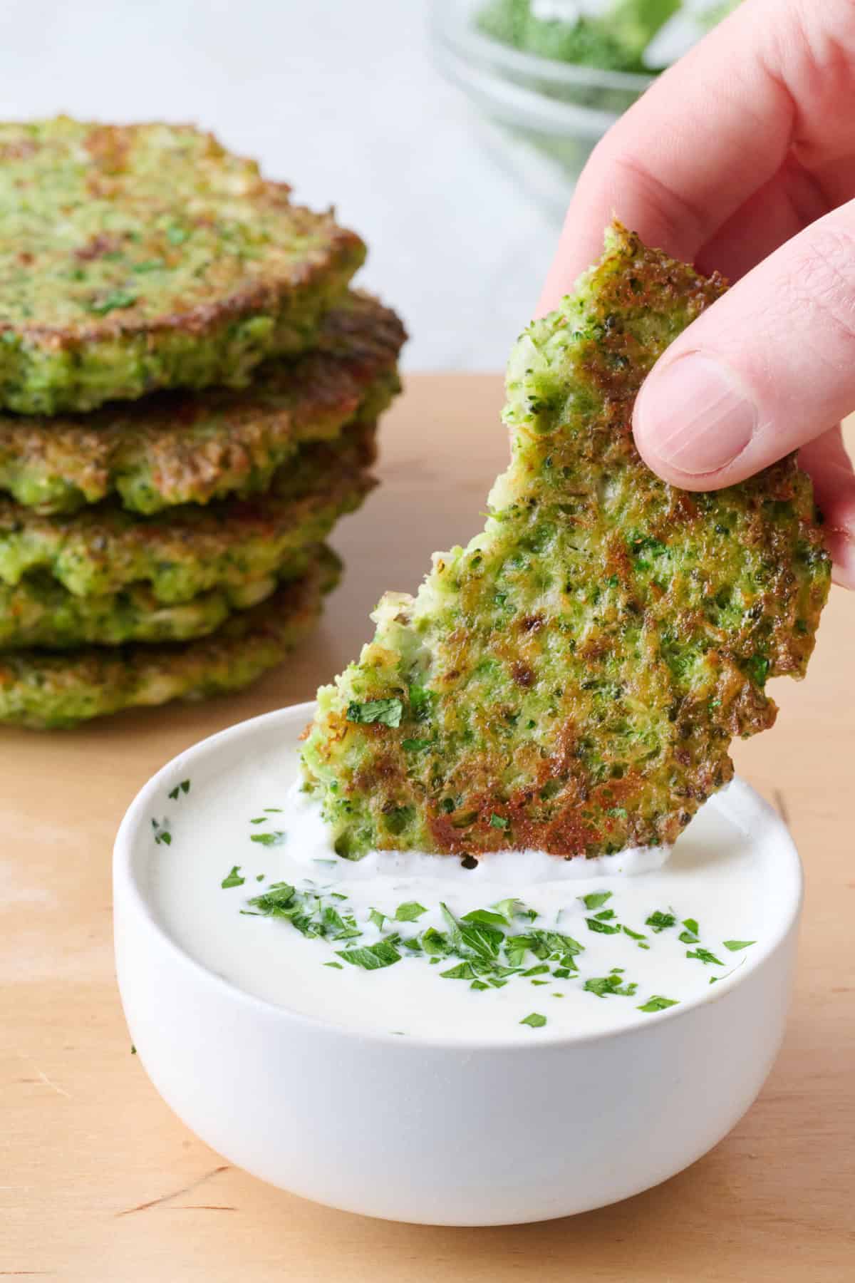 Hand dipping broccoli fritter in to Greek yogurt sauce.