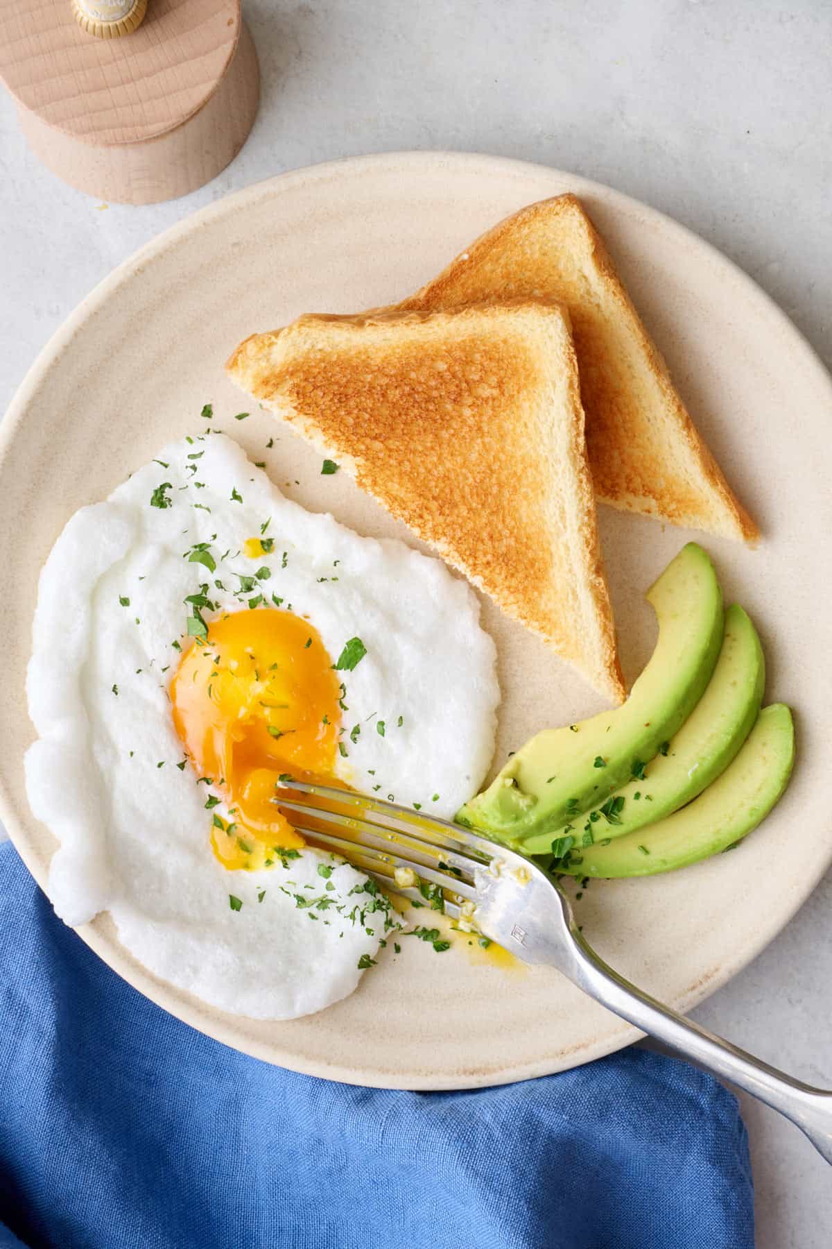 Microwaved cloud egg cut into on the plate with toast and avocado, yolk running.