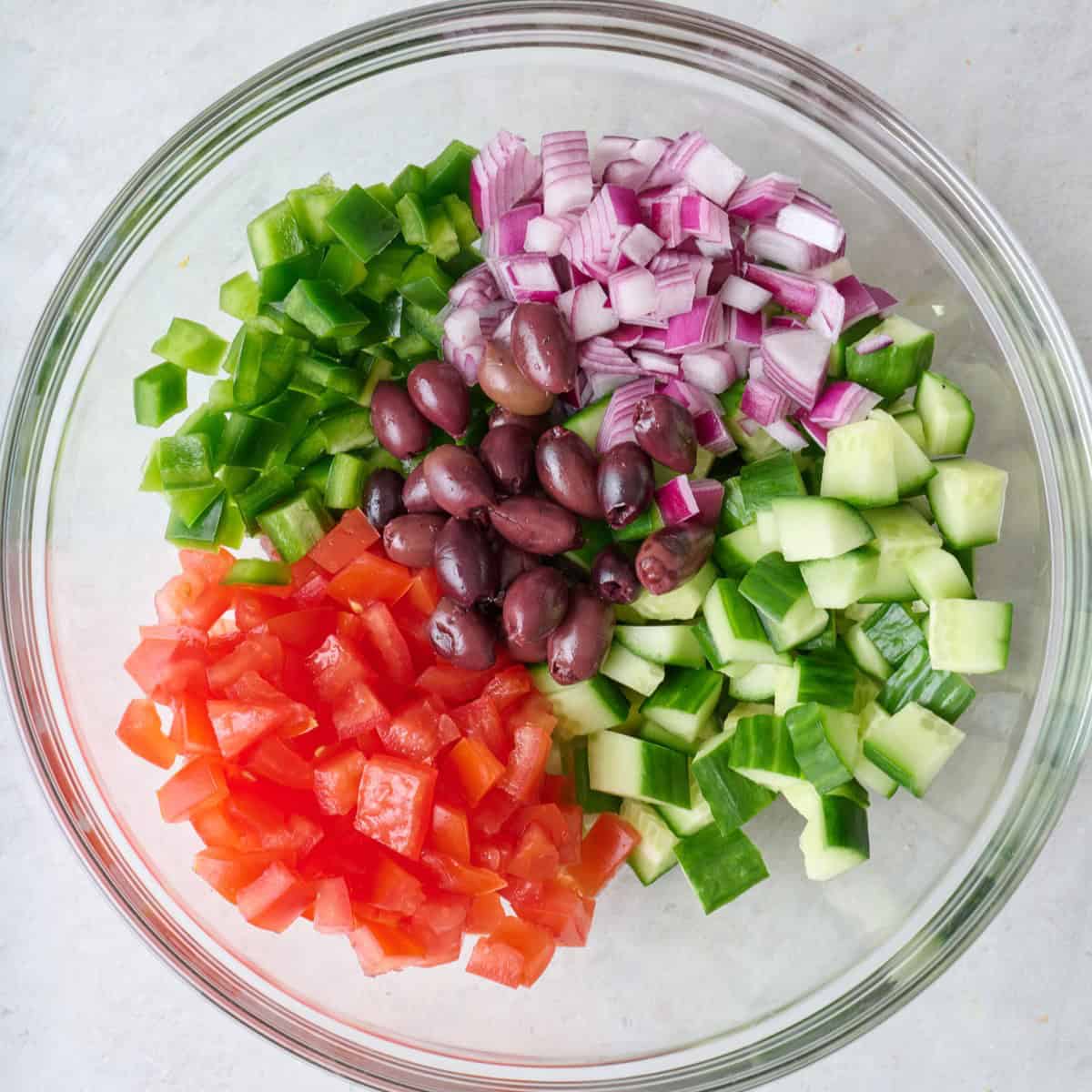 Diced tomatoes, cucumbers, red onions, bell pepper and olives in a bowl.