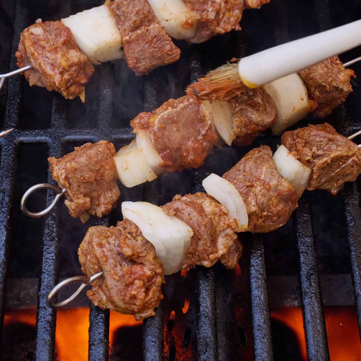 Lamb skewers on a grill, brushing leftover marinade on them.