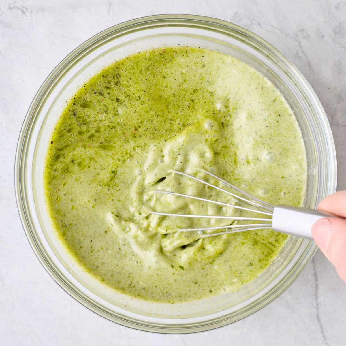 Whisking creamy pesto sauce in a bowl.