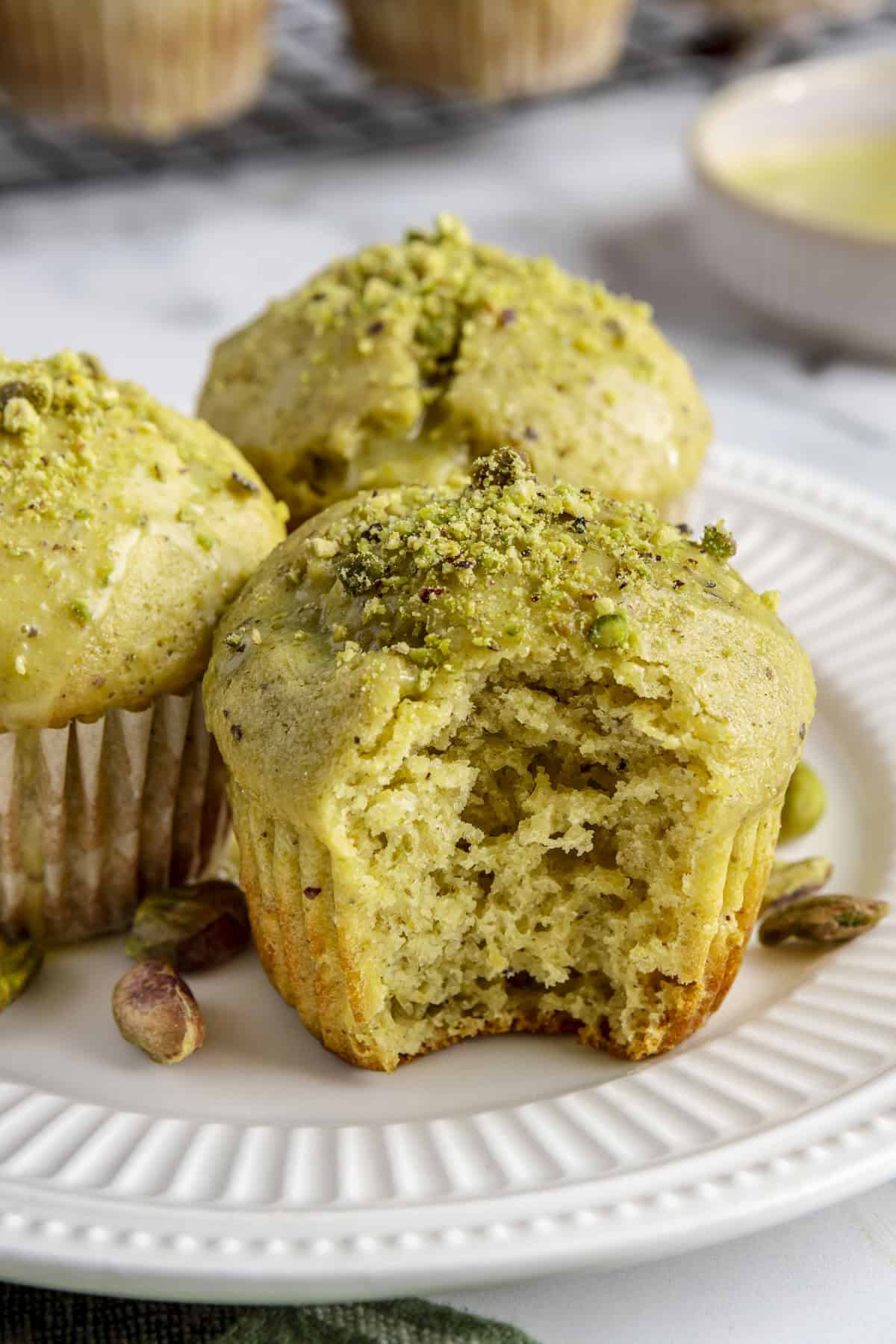 Homemade pistachio muffins on a plate with a bite taken out of one to show inside texture.
