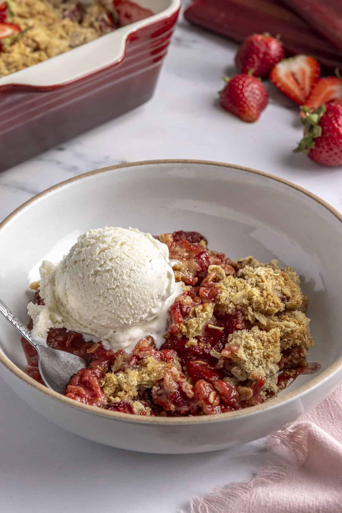 Serving of strawberry berry rhubarb crisp in a bowl with a scoop of ice cream on top.
