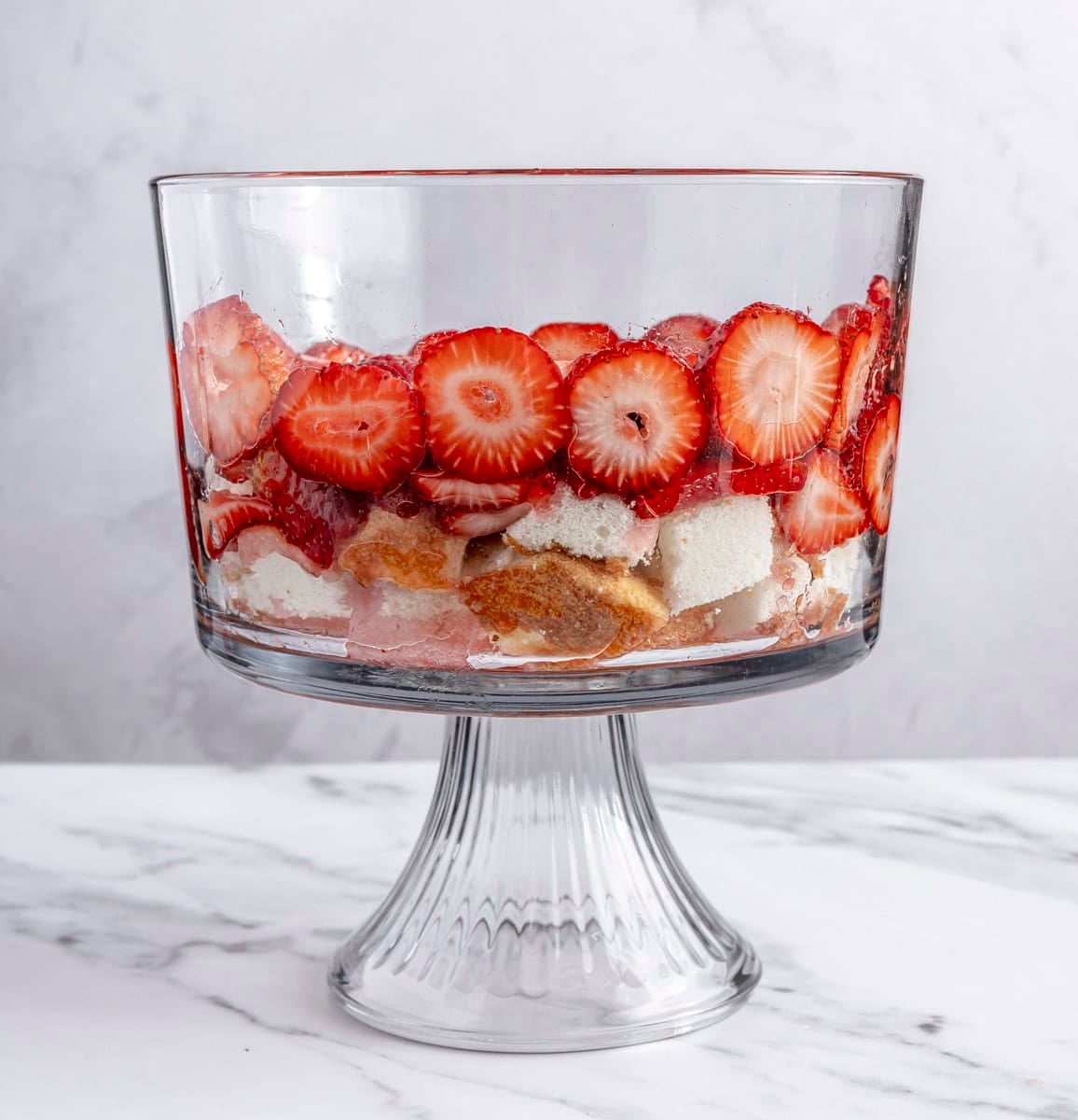 Sliced macerated strawberries and juices added on top of cake pieces.