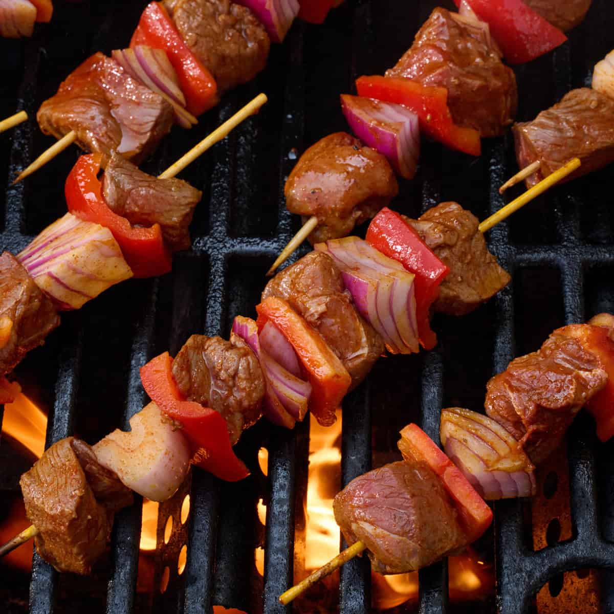 Skewers threaded with beef, peppers and onions on a grill.