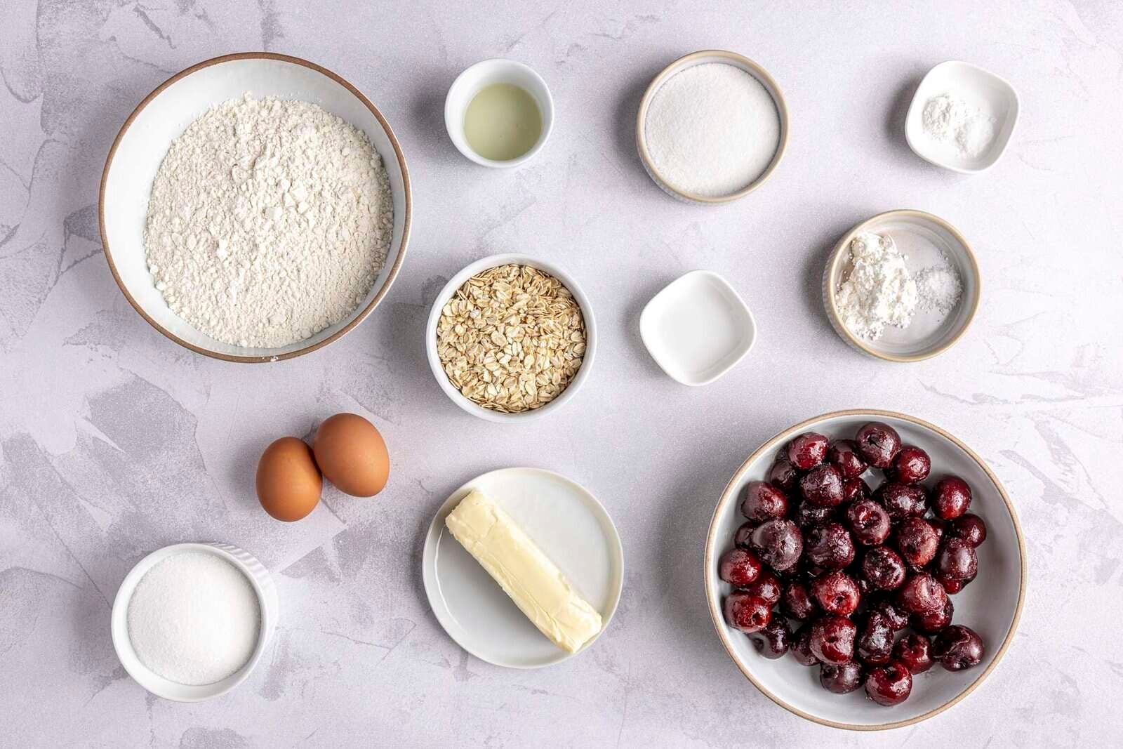 Ingredients for recipe: flour, lemon juice, sugar, cornstarch and salt, baking powder and salt, almond extract, oats, eggs, butter, frozen cherries, and sugar.