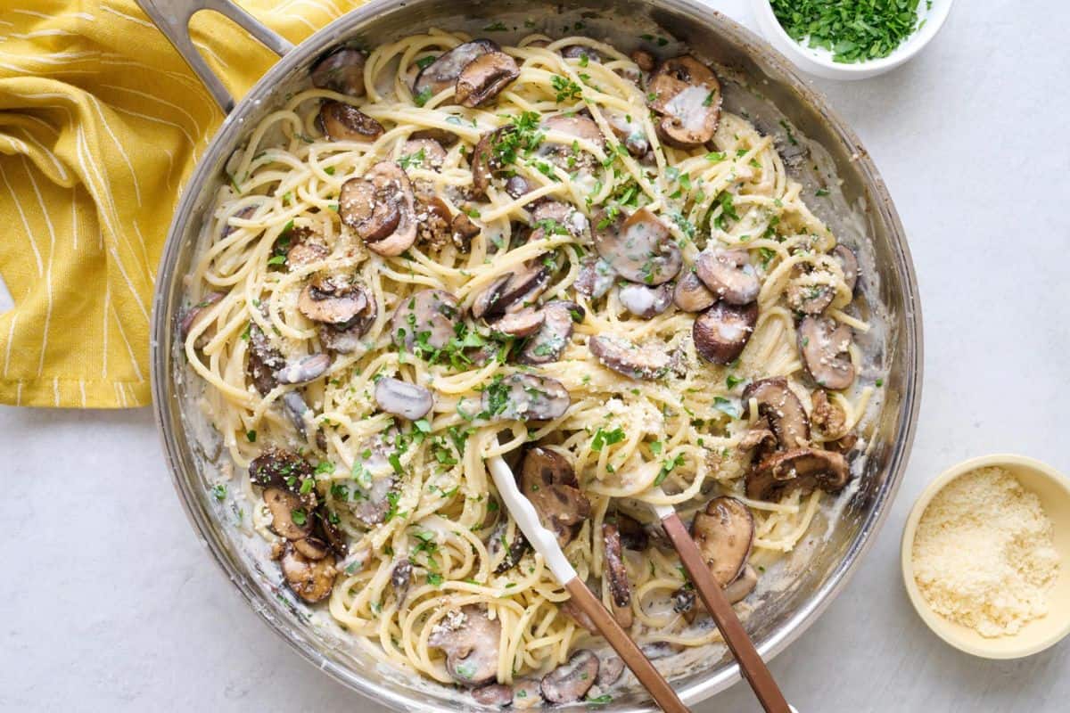 Easy creamy mushroom pasta recipe in a skillet with a small dish of grated parmesan nearby.
