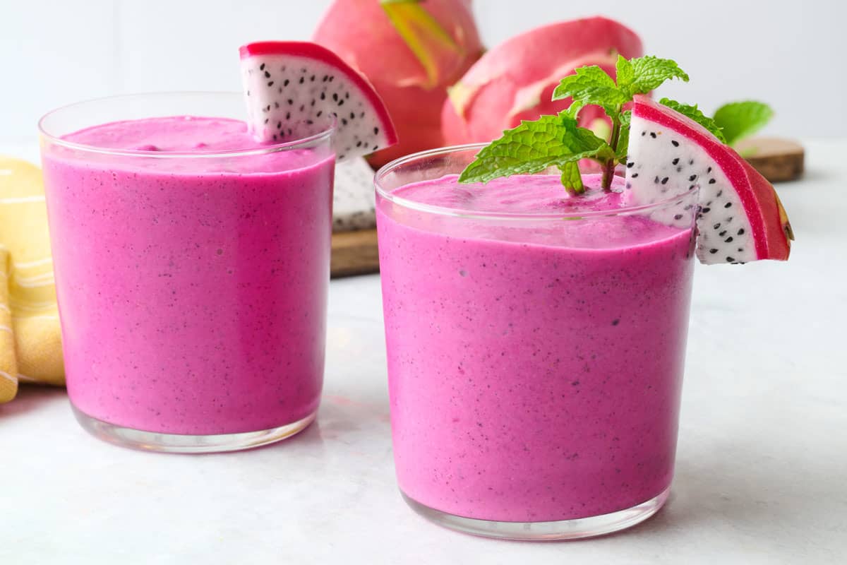 Two glasses of dragon fruit smoothie with a small wedge of fresh dragon fruit on each glass.