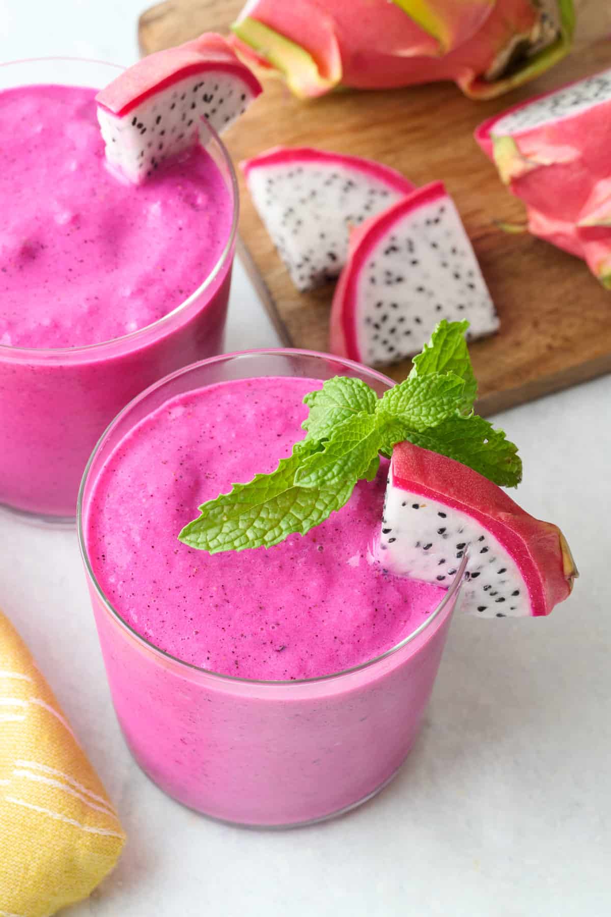 Bright pink dragon fruit smoothie in glasses with a small fresh dragon fruit triangle on rim with fresh mint.