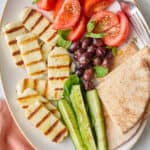 Grilled halloumi recipe on platter with fresh veggies, olives, and pita.