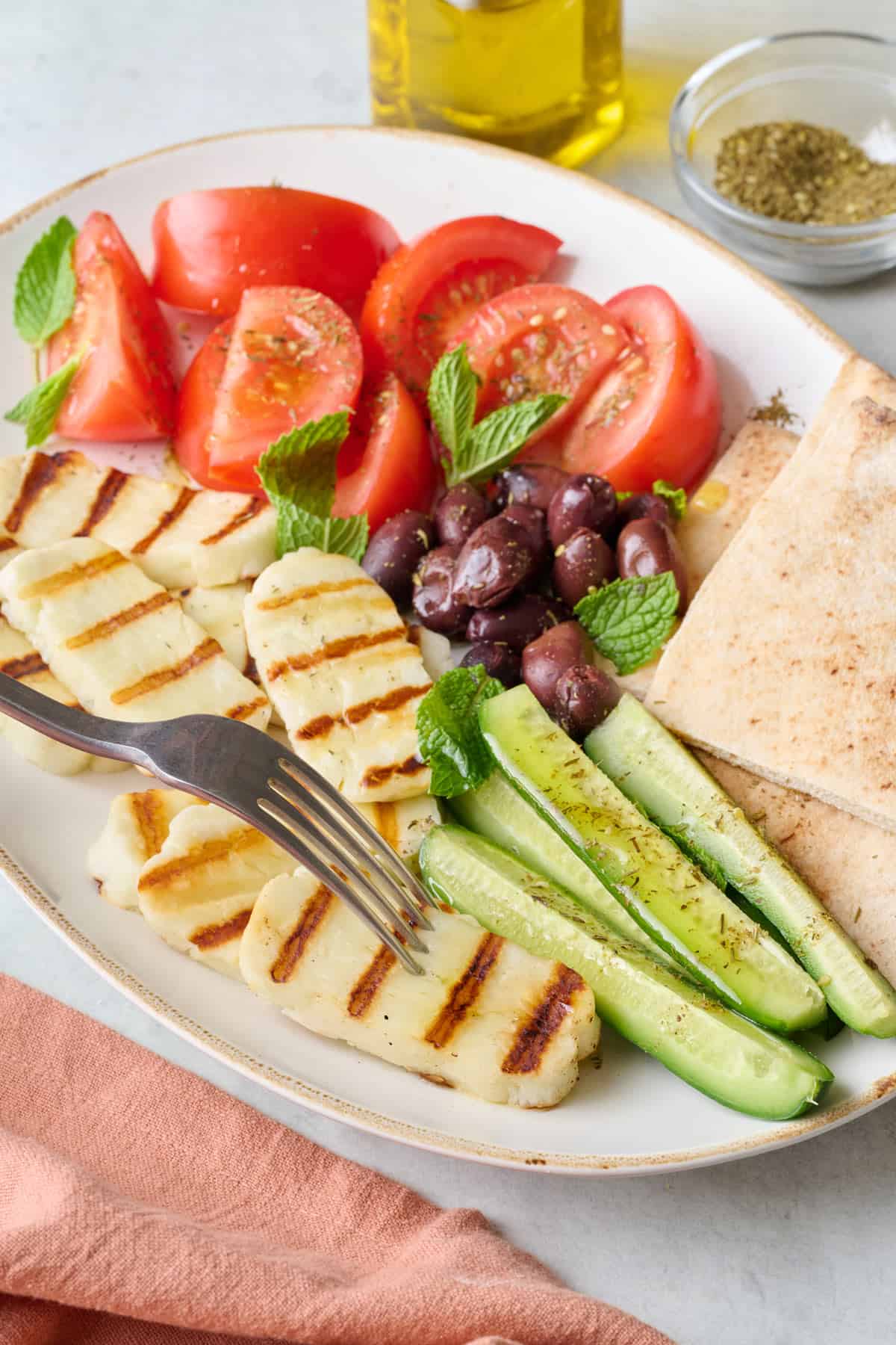 Grilled halloumi recipe on platter with fresh veggies, olives, and pita.