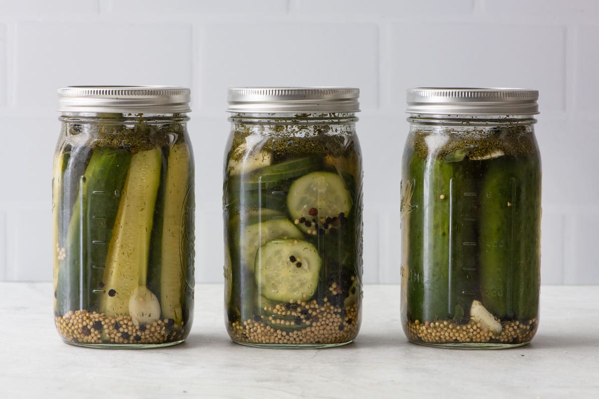 Three jars of homemade pickles in different cuts: spears, slices, and whole.
