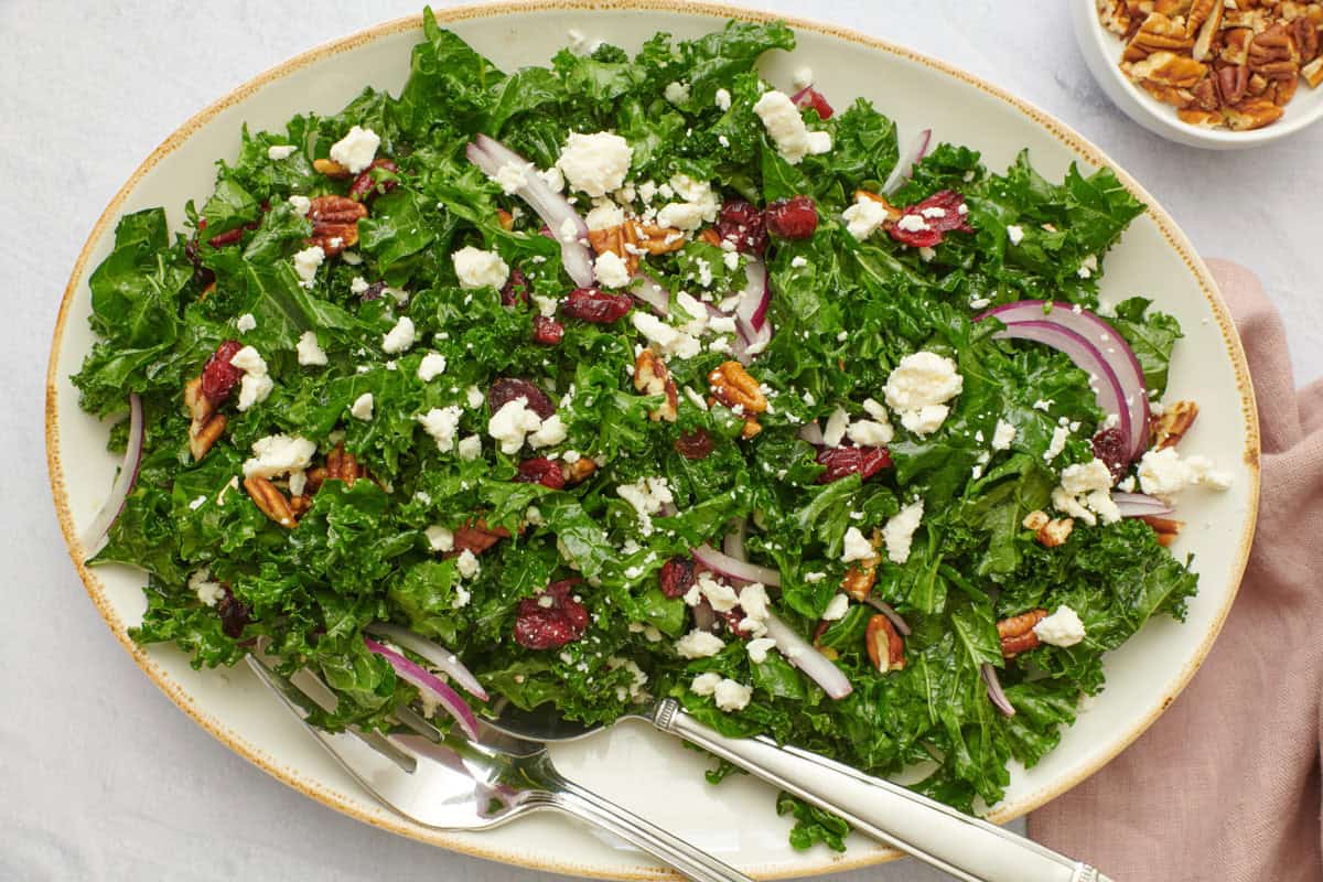 Massaged kale salad on a platter with crumbled feta, pecans, red onions, and dried cranberries.