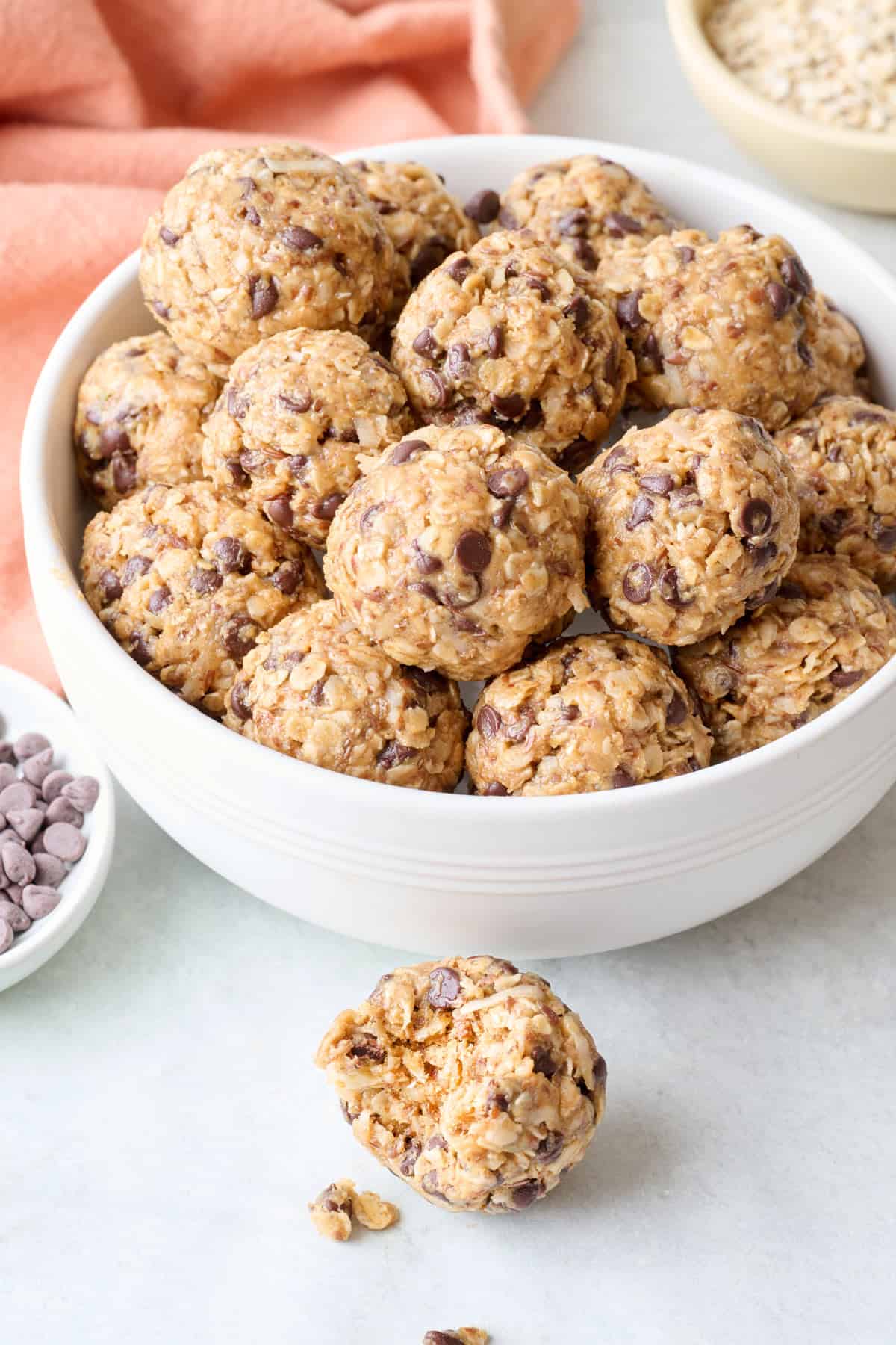 Bowl of no bake energy bites with chocolate chips in a bowl with one resting nearby with a bite taken out.