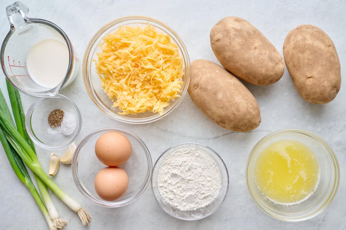 Ingredients for recipe: potatoes, cheese, milk, salt and pepper, green onions, garlic, eggs, flour, and melted butter.