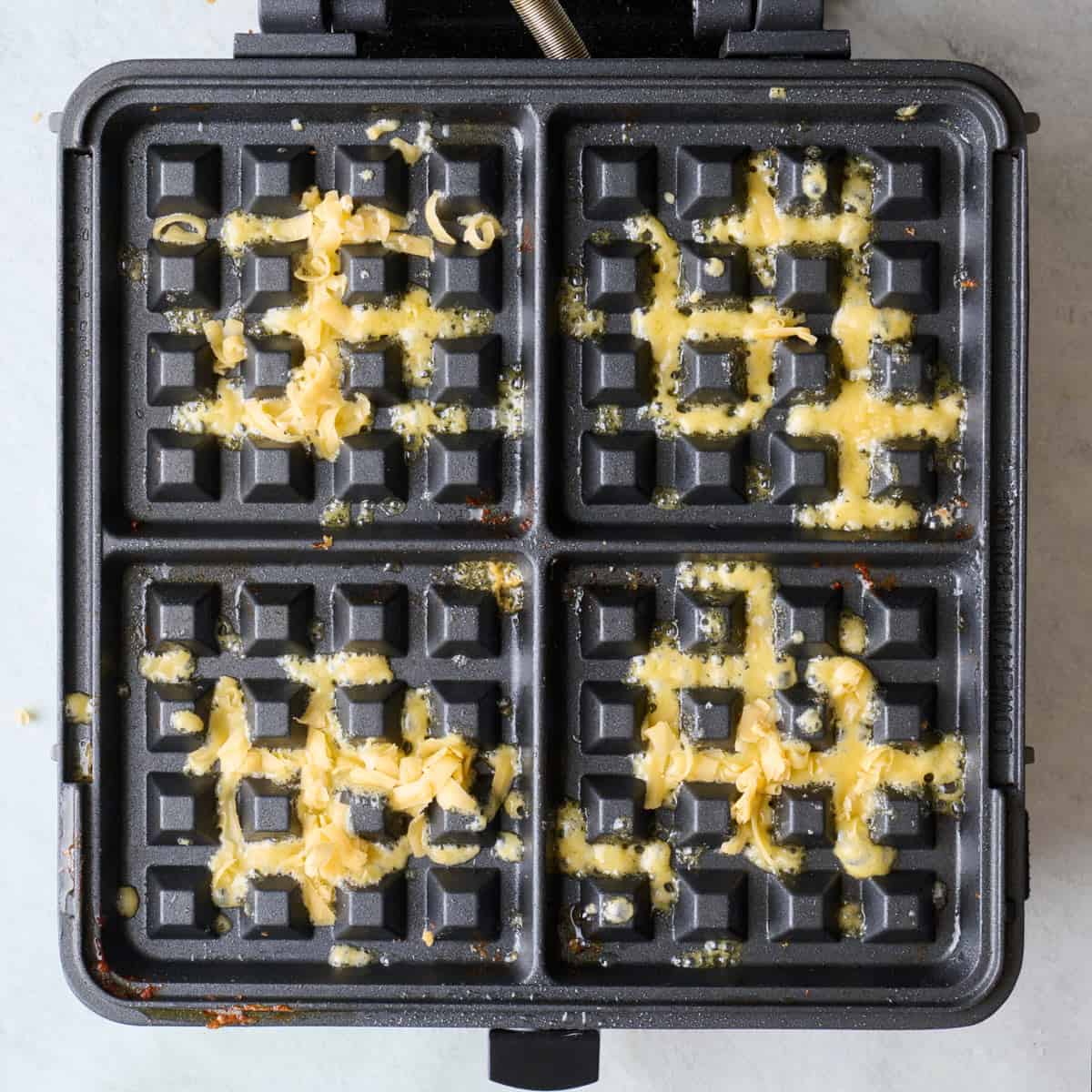 Waffle iron sprayed with oil and shredded cheese sprinkled on top.