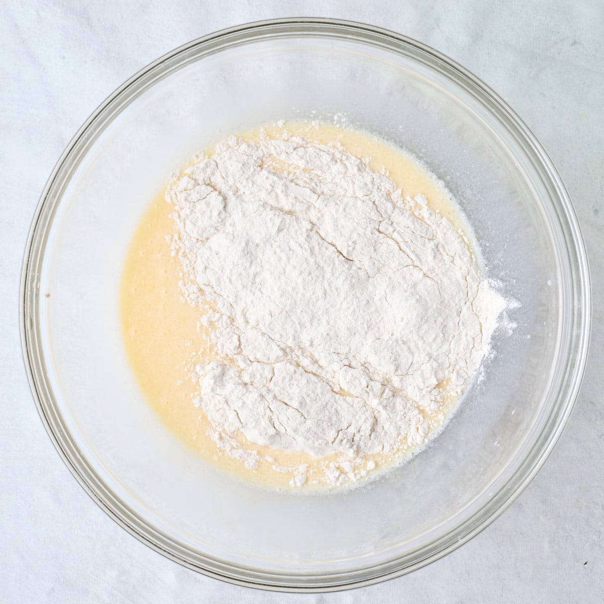 Whisked egg, milk, and butter in a bowl with dry ingredients added on top.