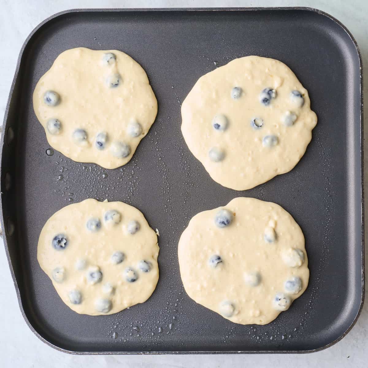 4 blueberry pancakes on a griddle before cooking.