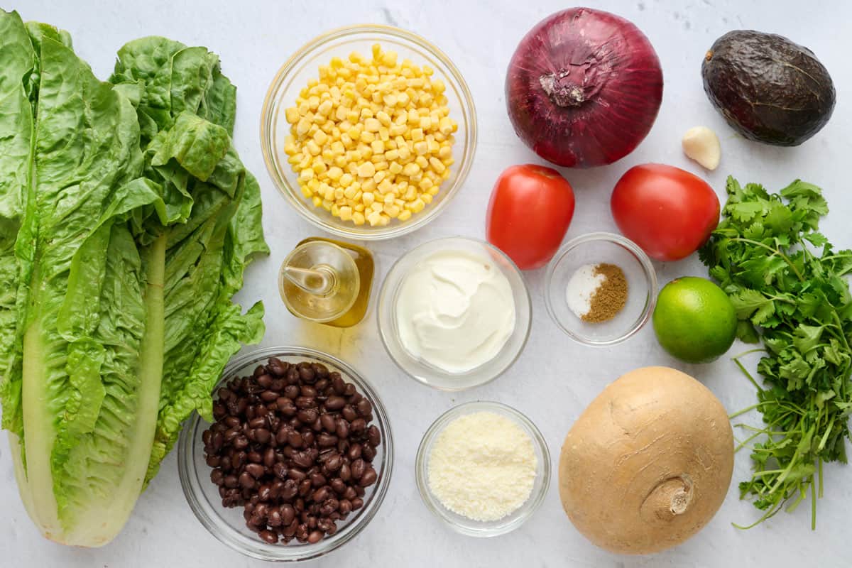 Ingredients for recipe before prepping: lettuce, corn, beans, oil, yogurt, cojita cheese, tomatoes, onions, avocado, garlic, lime, cilantro, and jicama.