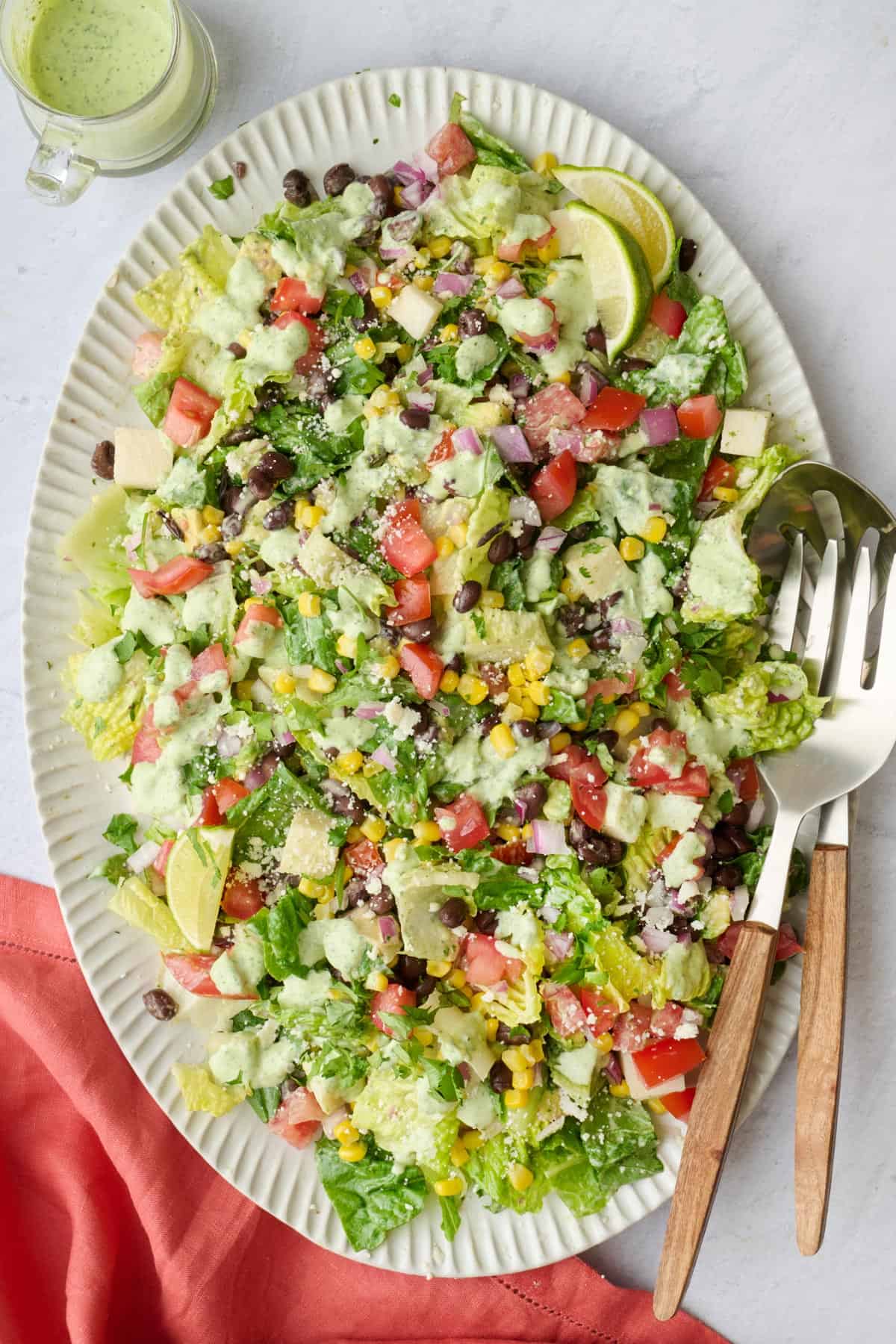 Tossed chopped mexican salad on a large platter with dressing drizzled on top.