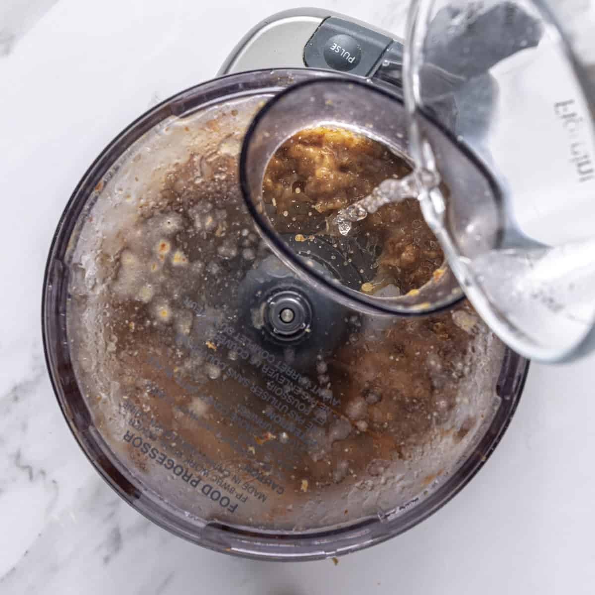 Pouring water into food processor while running.