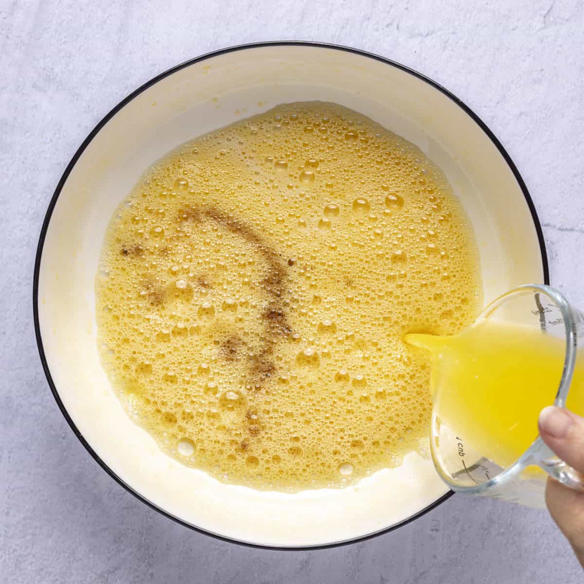 Light and foamy whisked eggs with milk and vanilla added and hand pouring in melted butter from the side of bowl.