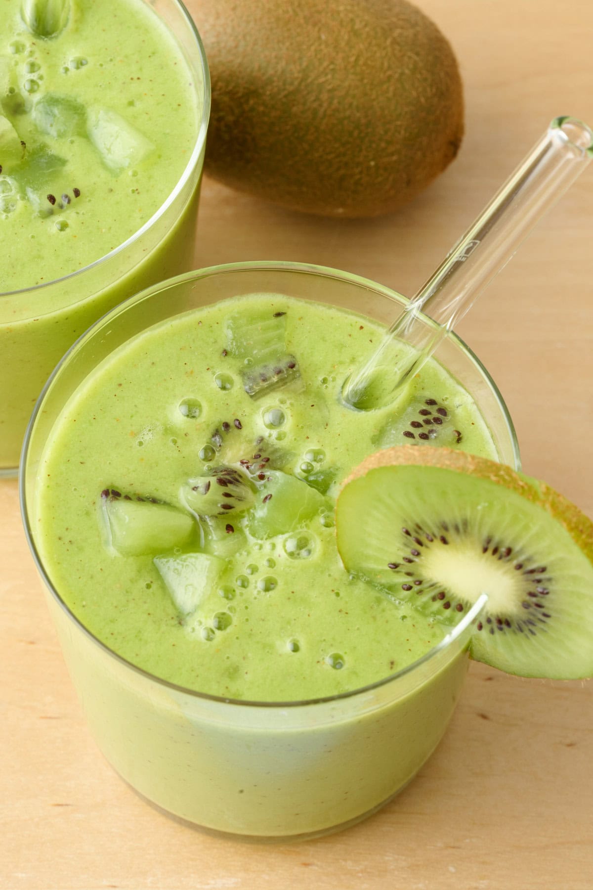 Creamy kiwi smoothie in a glass topped with fresh chunks of kiwi.