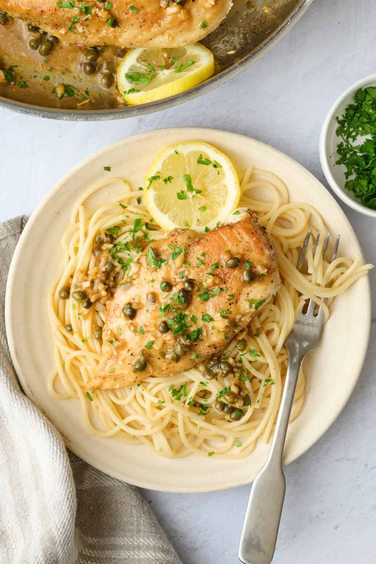 Serving of easy lemon chicken piccata served over pasta with extra lemon butter caper sauce on top.