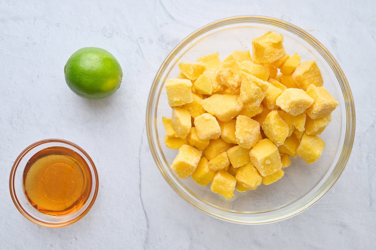 Ingredients for recipe: frozen mango chunks, lime, and maple syrup.