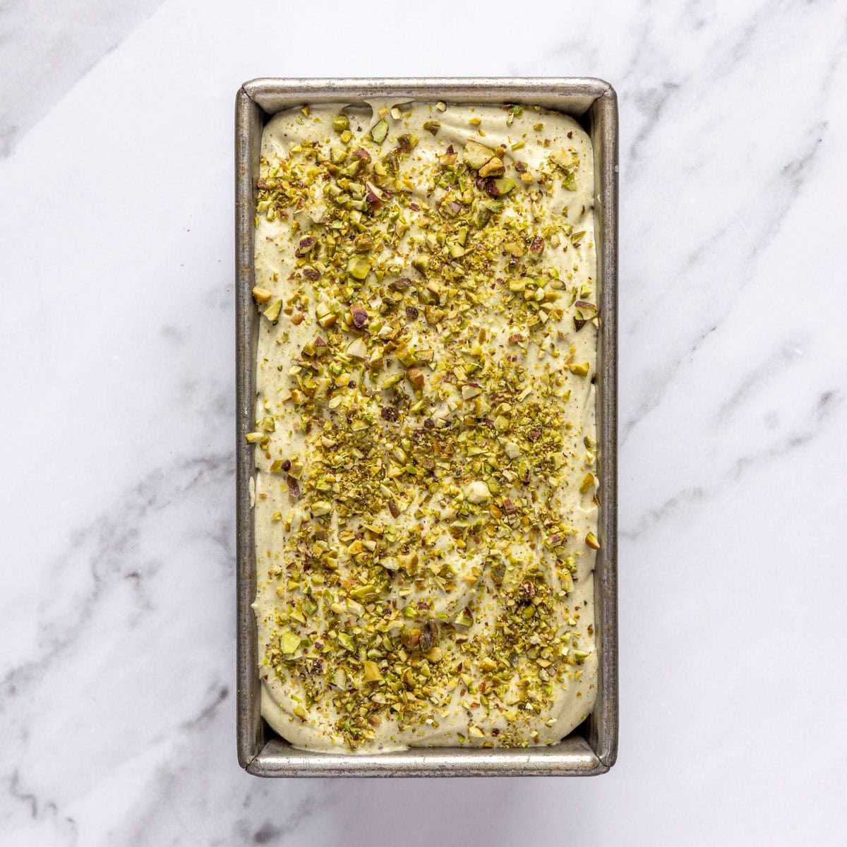 Pistachio ice cream in a freezer safe container topped with chopped pistachios.